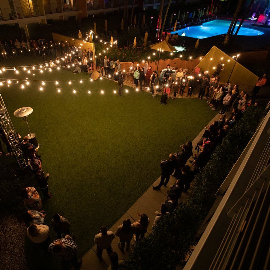 A circle of people gathered on a courtyard lawn under string lights for a cacao ceremony