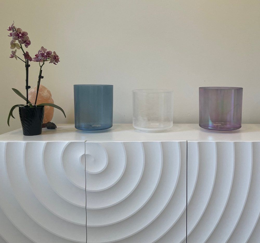 Crystal singing bowls arranged on a white cabinet beside an orchid